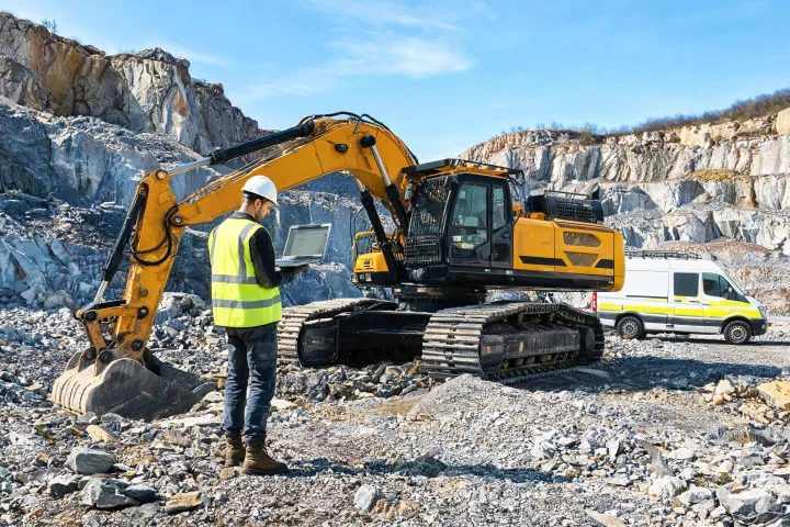 Field technician diagnosing excavator with laptop
